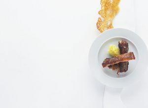 Travers de porc « laquépices », condiment pissaladière, cœur de laitue et grattons de socca